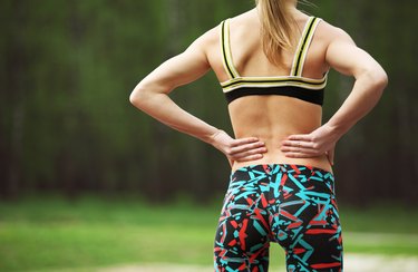 Athletic young woman rubbing muscles of lower back after jogging