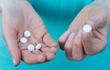 A close-up of two hands holding aspirin in one hand and vitamin K in the other.