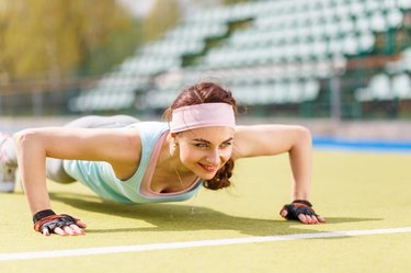 Young attractive woman doing push-up or core exercise on the grass field