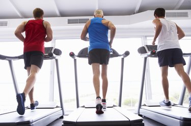 Back View Group Of Men Using Running Machines In Gym