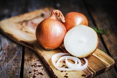 Whole and halved onions on a wooden cutting board.