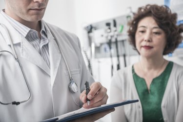 Doctor writing on medical chart with patient in the background
