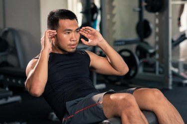 Vietnamese young man doing sit-ups on the bench