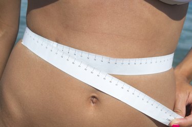 Girl measuring her waist at the seaside