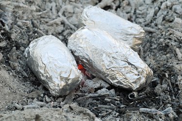 tin foil wrapped potatoes on hot coals in campfire