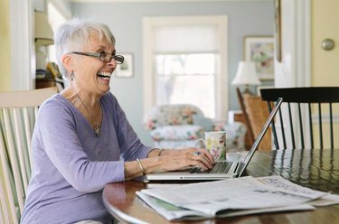 A senior woman smiling and working on a laptop at her kitchen table