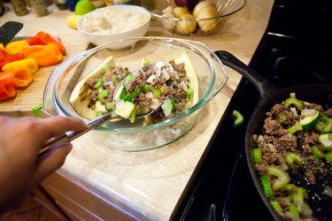 person scooping ground meat gilling into white eggplant shells