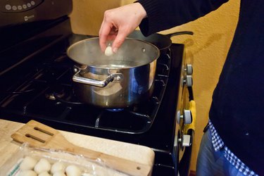 a hand dropping gnocchi into a pot of boiling water