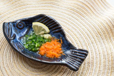 Fish-shaped serving bowl containing chopped peppers, grated carrot and a slice of fresh lemon.