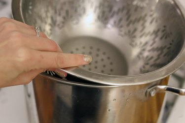 hand placing a steaming basket over a boiling saucepan of water