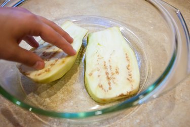 person coating white eggplant in olive oil