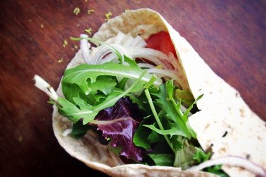 Close view of a wrap with hummus and vegetables on a wooden table