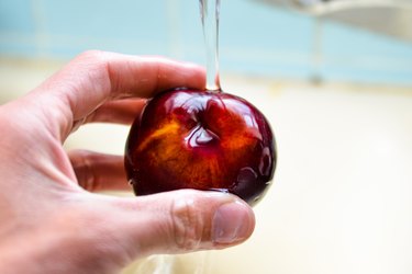 hand washing whole plum under running water