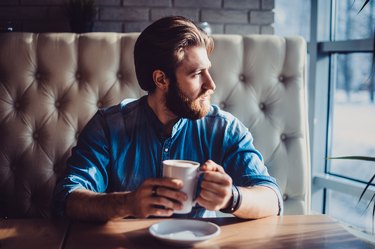 man sitting at cafe with coffee not eating staring out the window