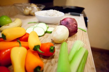 cutting board on kitchen counter with veggies like bright red and yellow peppers, onions and celery.