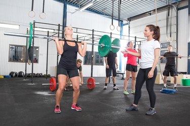 woman lifting weights in the gym as her trainer watches