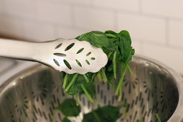 tongs removing steamed spinach from basket