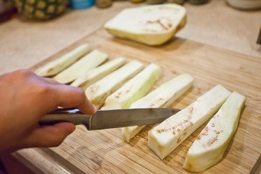person cutting white egg plant on cutting board with a knife