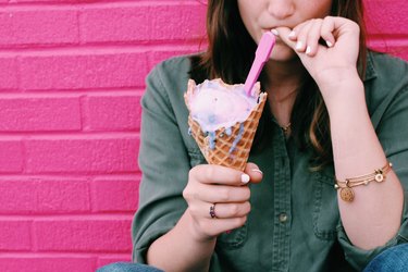 Close up of a person with brown hair and a long sleeve green shirt holding an ice cream cone with a spoon, showing up she's giving up emotional eating for good.