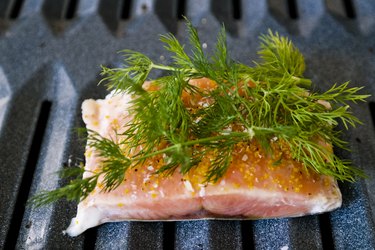 Salmon with fresh herbs on top on a broiler pan in the oven