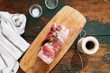 Raw lamb flaps on a wooden cutting board, wrapped in butcher's twine, ready to be cooked