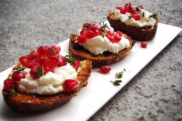 A white plate with three bruschetta topped with ricotta and pomegranate seeds