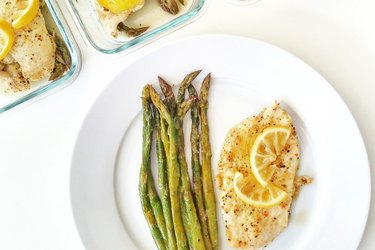 Top view of a plate with grilled chicken breast topped with lemon and a side of asparagus