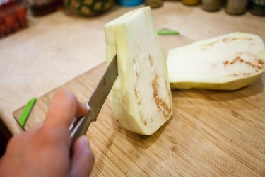 Person slicing white eggplant on a cutting board