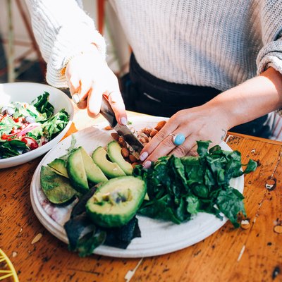 Woman chopping salad and avocados on a plate.