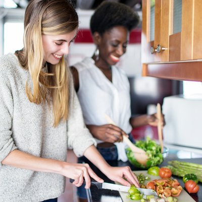 Two women cutting vegetables in kitchen