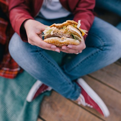 Tasty burger in woman’s hands. Takeaway junk food top view. Unhealthy meals and hurry eating, friendship and sharing time together concept
