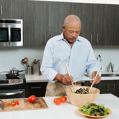 An older man making a salad in his kitchen