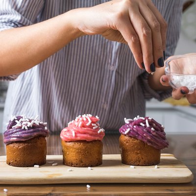 Woman putting sprinkles on sugary cupcakes