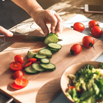 Woman chopping veggies for the Noom Diet with the app open on her phone next to her
