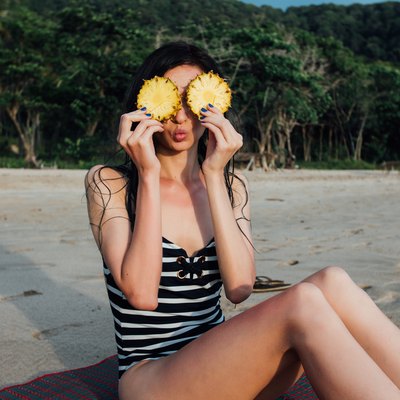 woman sitting on a beach playing with pineapple slices