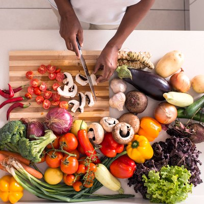 Woman on a weight-loss diet chopping a variety of vegetables in her kitchen