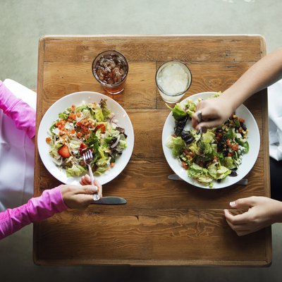 Overhead shot of two women eating salads at a restaurant practicing portion control