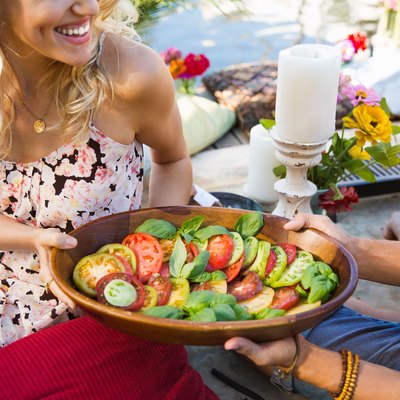 Man and woman passing a tomato salad at a summer picnic