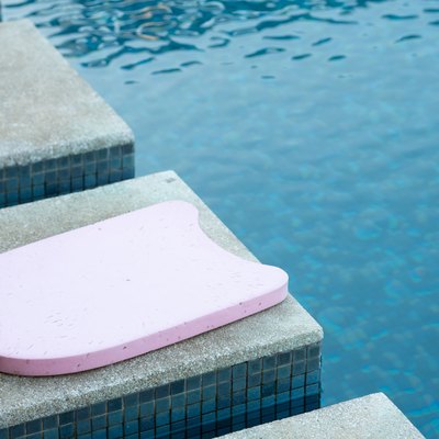 Pink kickboard by the side of a pool to help teach swimming lessons to become a better swimmer