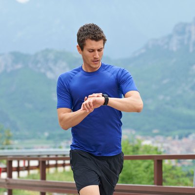 Man running outside in the mountains looking at running watch.