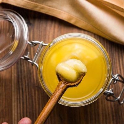 Ghee, or clarified butter, in glass or copper container or ceramic jar with spoon, selective focus