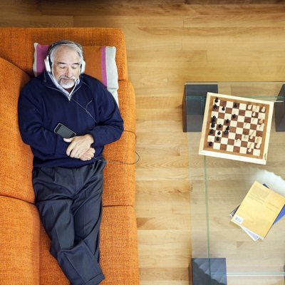 Older man resting on orange couch and listening to music during colonoscopy recovery