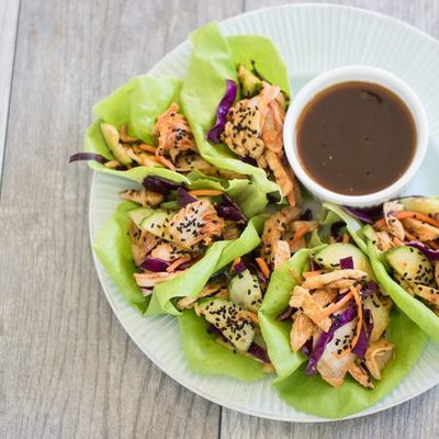 A plate of lettuce cups with kimchi and grilled chicken, and a dipping sauce on the side