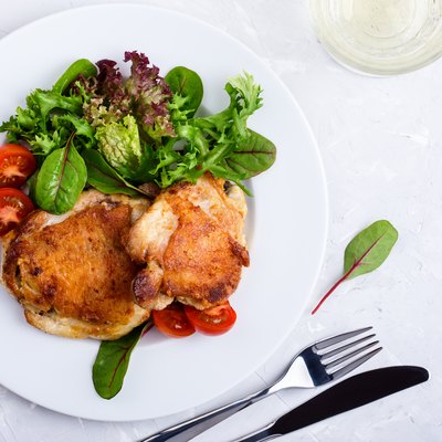 Roast chicken legs on white plate over light gray plaster texture table