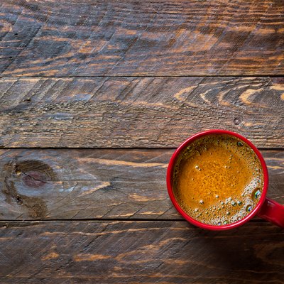 Red mug with freshly brewed coffee with appetizing crema on aged wood kitchen table. Cozy winter fall holiday atmosphere copy space