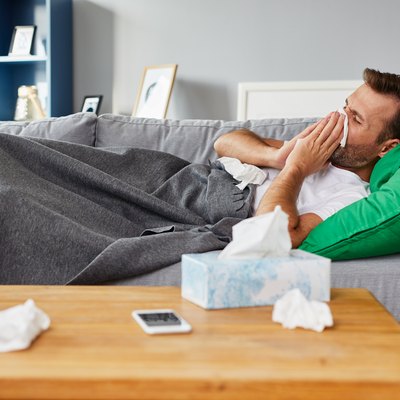Sick man lying on sofa at home and blowing nose