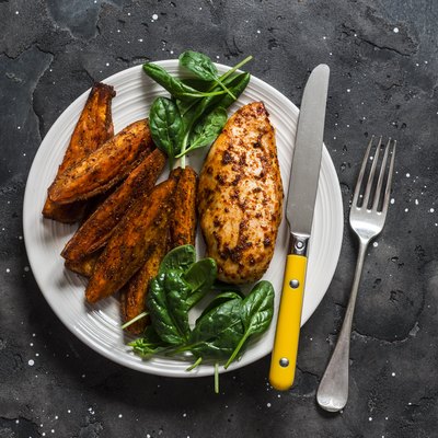 Baked chicken breast with sweet potatoes and spinach on a dark background, top view. Balanced healthy lunch