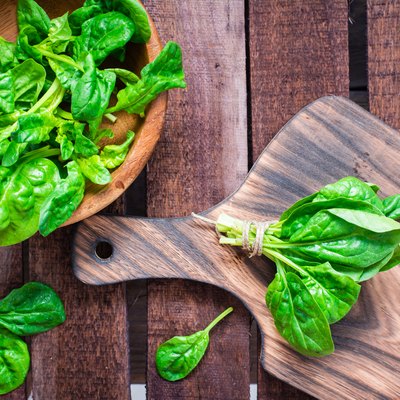 A bunch of fresh baby spinach leaves on a cutting board and spinach leaves in a bowl on a wooden table.