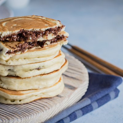 Stack of stuffed chocolate nutella pancakes on vintage wooden board on blue table background with cup of tea. American Breakfast Concept. Copy space