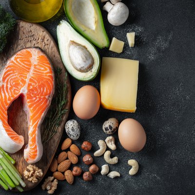 A set of healthy food for keto diet on a dark background. Fresh raw salmon steak with flax seeds, broccoli, avocado, chicken eggs, nuts and asparagus on a wooden Board. Top view with copy space